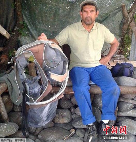 圖為當(dāng)?shù)貢r間7月30日，留尼旺島上的一名海岸清潔人員展示他找到的一個手提箱的殘骸。